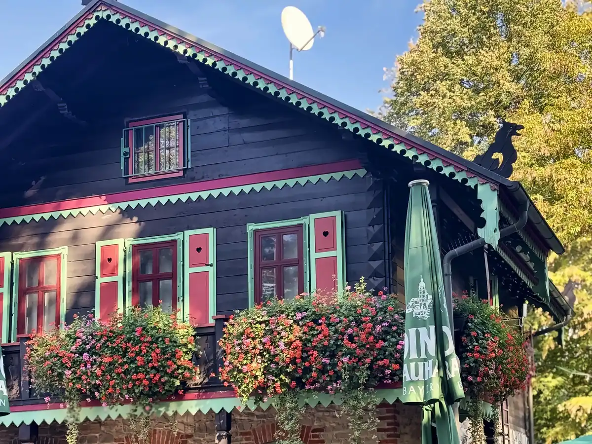 Fassade des Forsthauses Leiner Berg mit grün-roten Fensterläden und üppigen Geranien am Holzbalkon