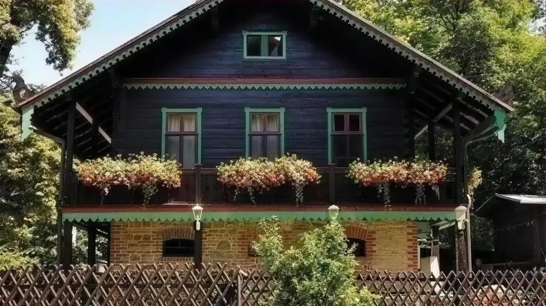 Das Forsthaus Leiner Berg – dunkles Holzhaus im Schweizer Stil mit grünen Fenstern und Blumenkästen, umgeben von Bäumen
